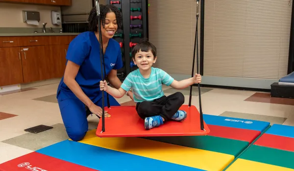 Occupational Therapist Assistant and young boy on swing demonstrating therapy for Occupational Therapy Month
