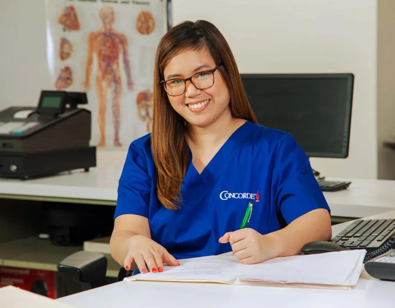 A medical office professional sitting at desk with pen completing paperwork.