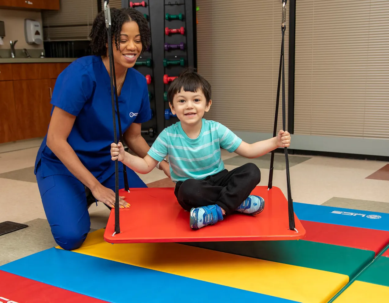 Occupational Therapist Assistant and young boy on swing demonstrating therapy for Occupational Therapy Month