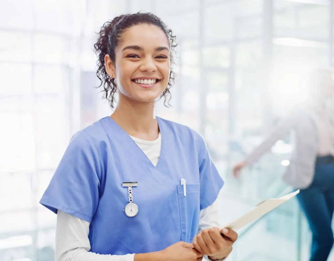 Medical assistant holding a clipboard and smiling in a modern healthcare facility.