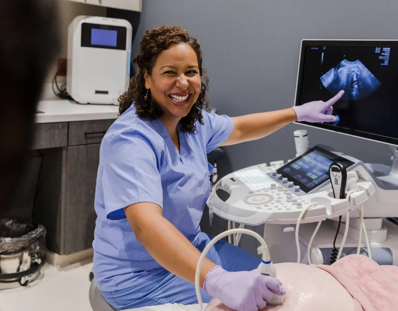 Smiling healthcare professional in scrubs performing an ultrasound scan and pointing to the fetal image on the monitor