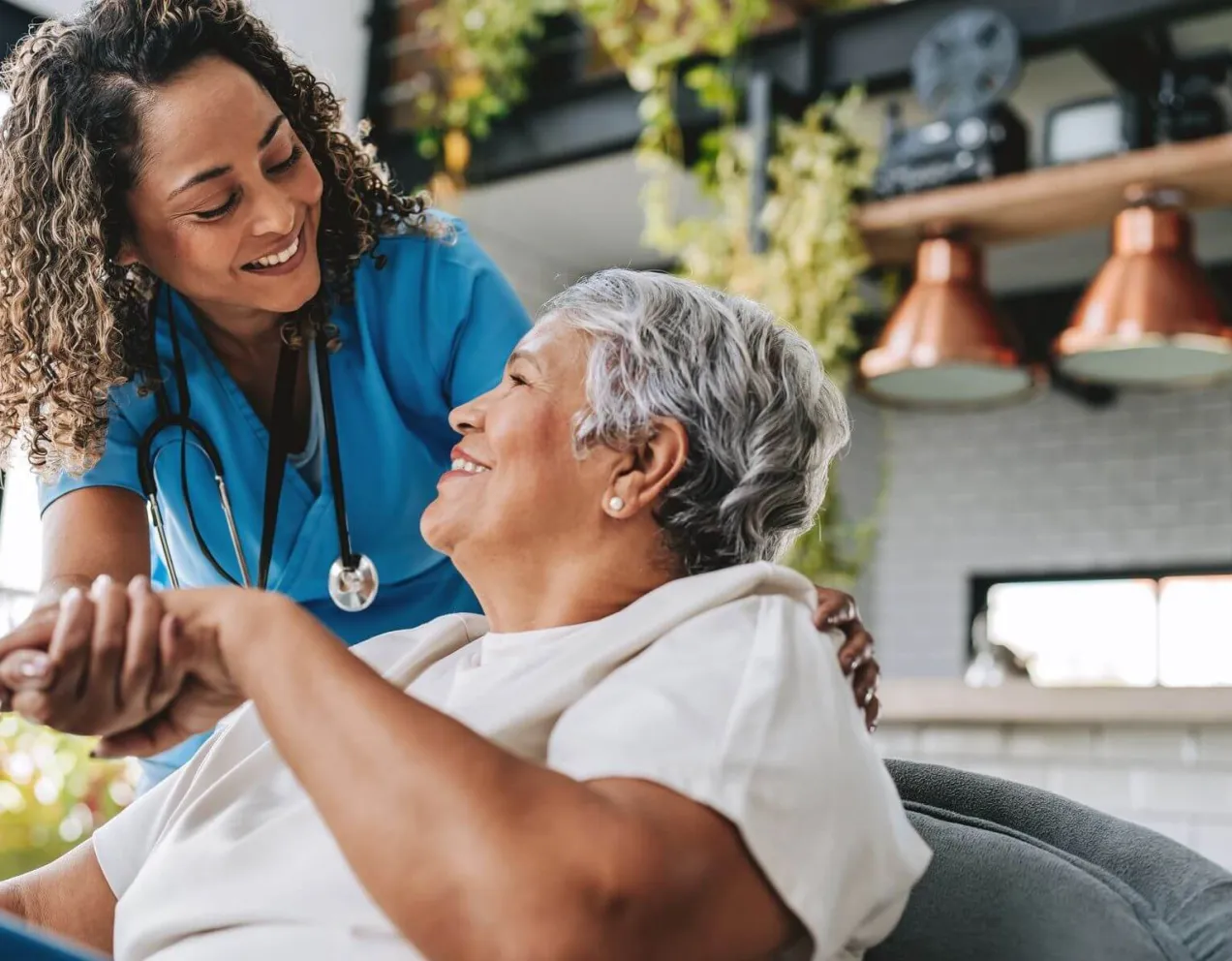 A smiling nurse holds the hand of an elderly patient in a warm, bright room, illustrating the rewarding patient-care aspect of changing your career to nursing.