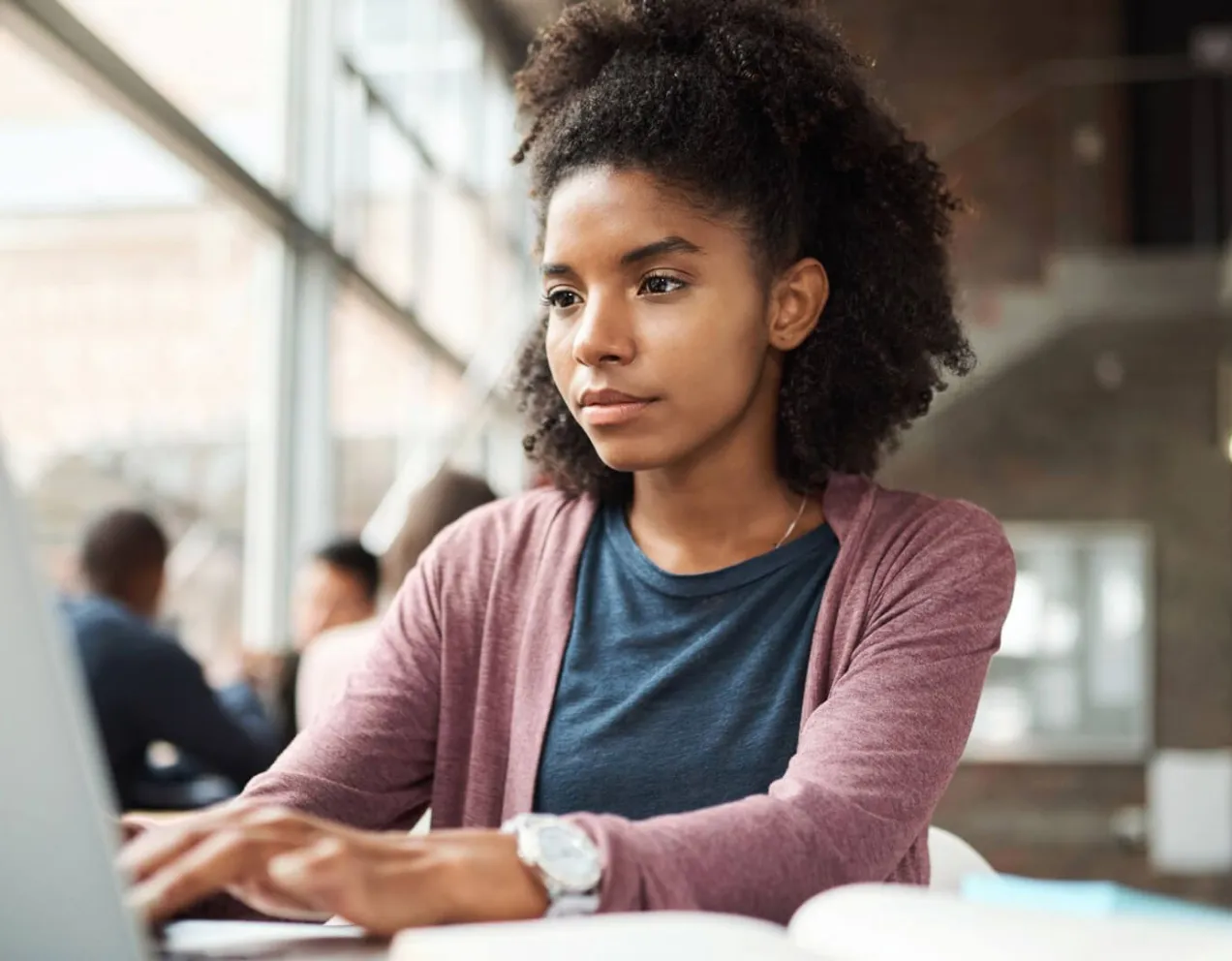 A focused young woman using a laptop in a bright study area to research FAFSA deadlines and submit her financial aid application online.