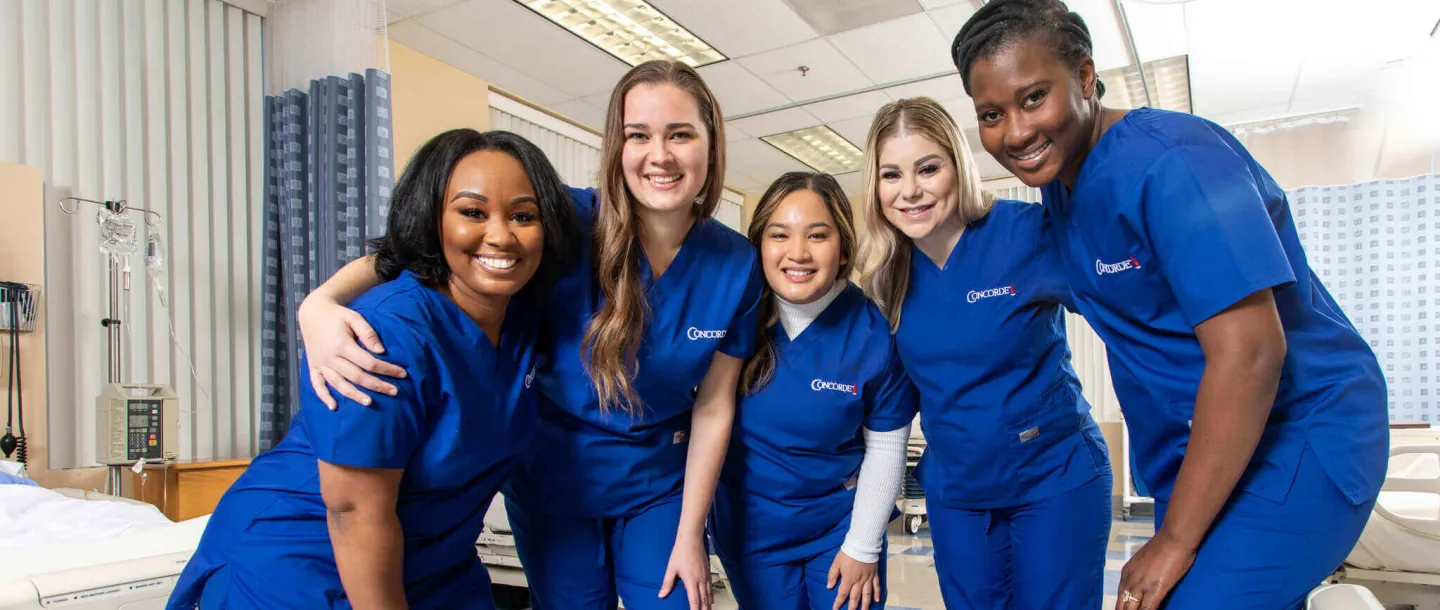 5 smiling Concorde graduates in blue scrubs in lab setting symbolizing student culture for high school open house