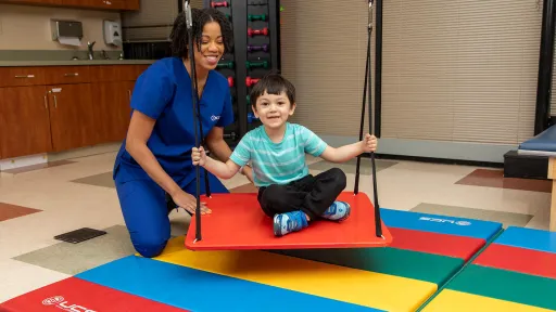 Occupational Therapist Assistant and young boy on swing demonstrating therapy for Occupational Therapy Month