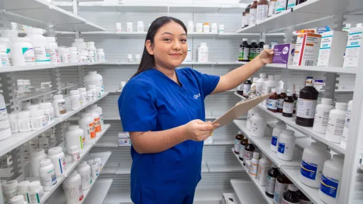 Pharmacy technician organizing medication on shelves with a clipboard.