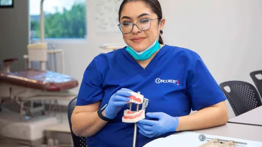 Lindsay sitting in a classroom holding a model set of teeth to practice dental assisting skills.