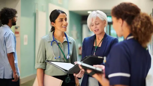 Healthcare administrator collaborating with medical staff in hospital hallway, discussing patient care and daily operations.