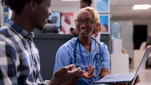 Medical assistant in scrubs discussing intake with patient, representing job duties and clinical work environment.