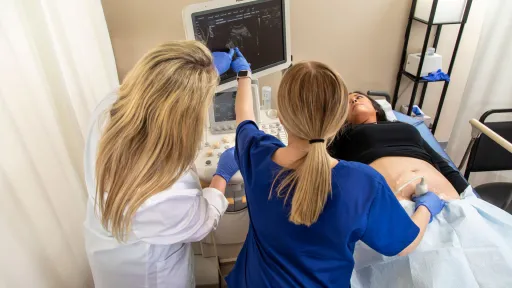 Instructor guiding sonography student during hands-on ultrasound training with patient.