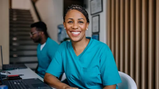 Medical assistant student in scrubs smiling at desk, representing degree and training options in health care careers