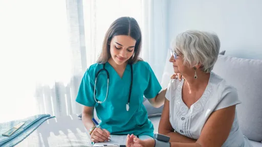 Medical assistant checking a patient’s blood pressure and recording notes.