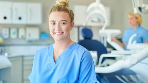 Dental assistant in scrubs standing in a dental office, representing the supportive role in patient care and procedures