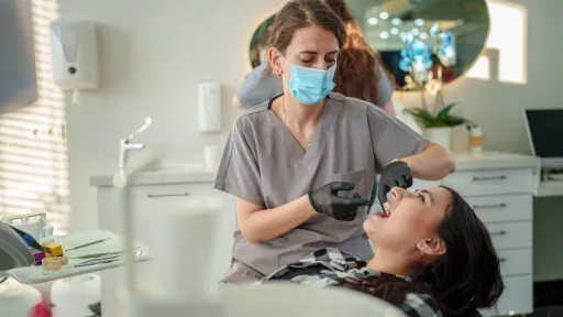 Dental hygienist in gray scrubs wearing gloves and mask while examining patient’s teeth