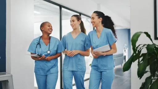 Practical Nursing to RN students in scrubs discussing charts as they walk through a hallway