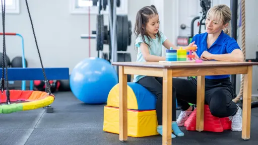 Occupational therapy assistant guiding a child in fine motor skill activities with stacking toys during a pediatric therapy session.