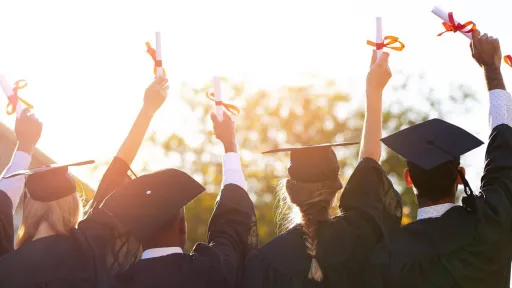 High school graduates looking thoughtfully to the future while raising their diplomas in the air