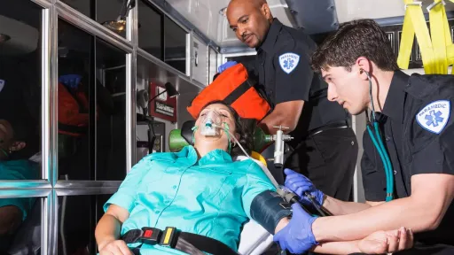 Male paramedics take blood pressure of patient on a stretcher in ambulance