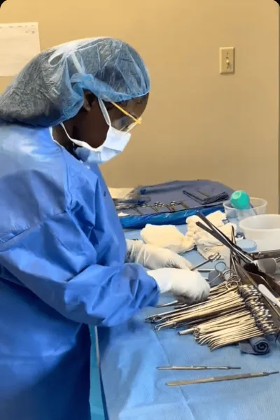 female surgical technologist wearing blue scrubs, face mask and surgical cap prepares surgical instruments for surgical procedure
