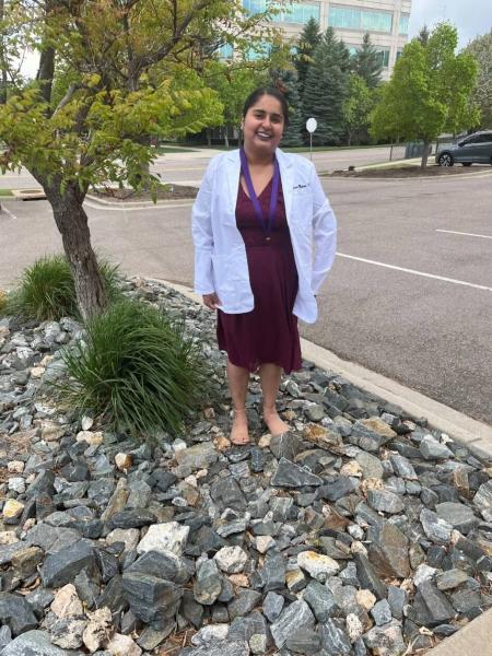 Julissa in a white lab coat standing outside in front of a tree.