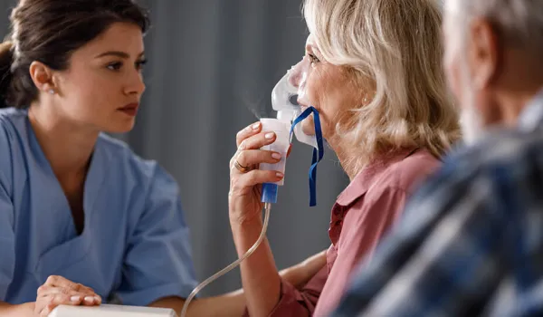 respiratory therapist gives breathing treatment to older woman