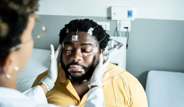 A polysomnographic technologist places electrodes on a patient's head to prepare him for a sleep study.