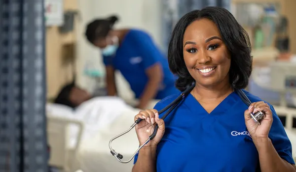 LPN in scrubs smiles while holding her stethoscope. 