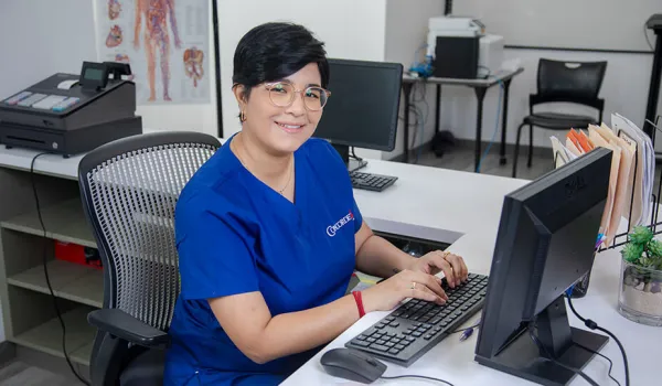 A smiling medical office professional at desk with her hands on keyboard.