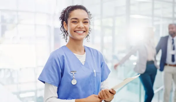 Medical assistant holding a clipboard and smiling in a modern healthcare facility.