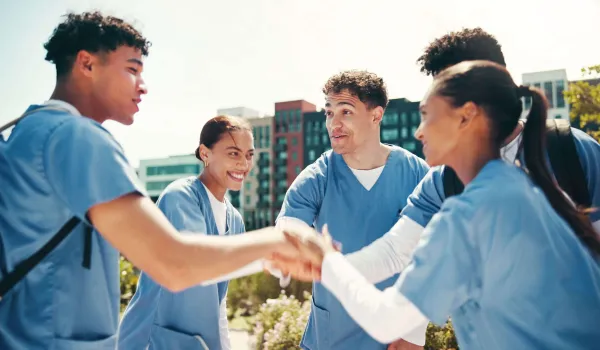 A group of nursing students in scrubs standing together and offering each other encouragement and peer support.