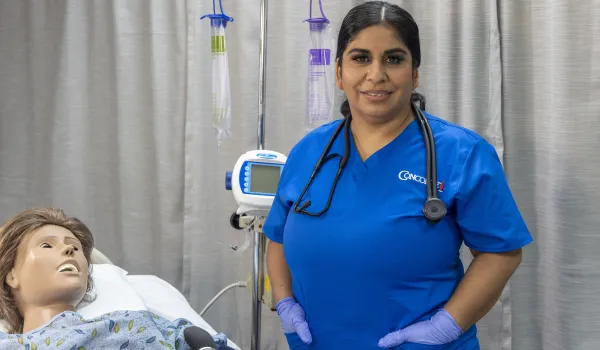 A female nurse with dark hair and blue scrubs poses for camera in lab setting