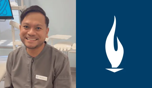 A male dental assistant with brown hair and wearing grey scrubs smiles for camera