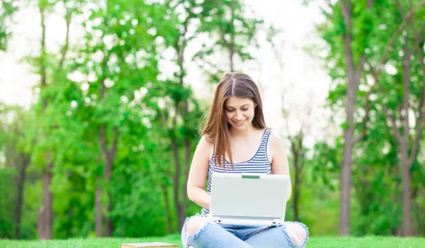 female teenager high school graduate researching on laptop outside during summer