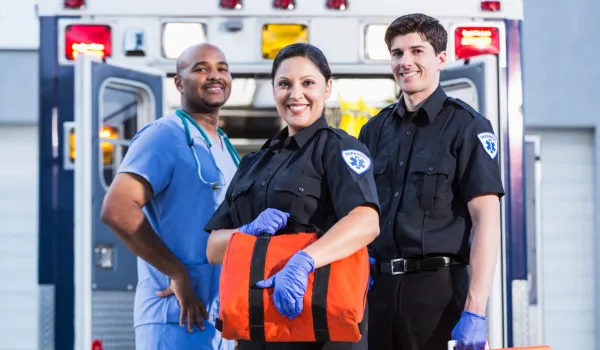 First responders, two paramedics and a healthcare worker, pose in front of and ambulance