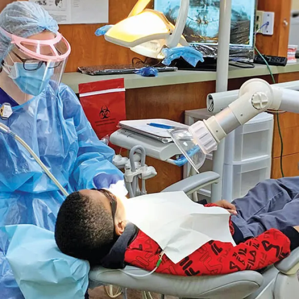 A dental hygienist performs a routine cleaning on young male patient.