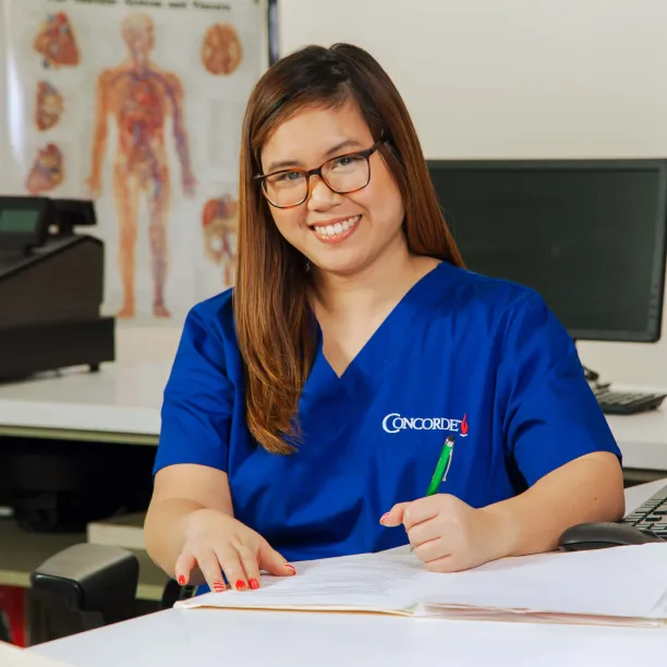 A medical office professional sitting at desk with pen completing paperwork.