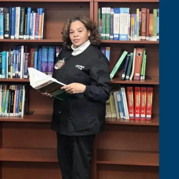Selinza Mitchell holding a book in the learning resource center next to an image of the Concorde logo.