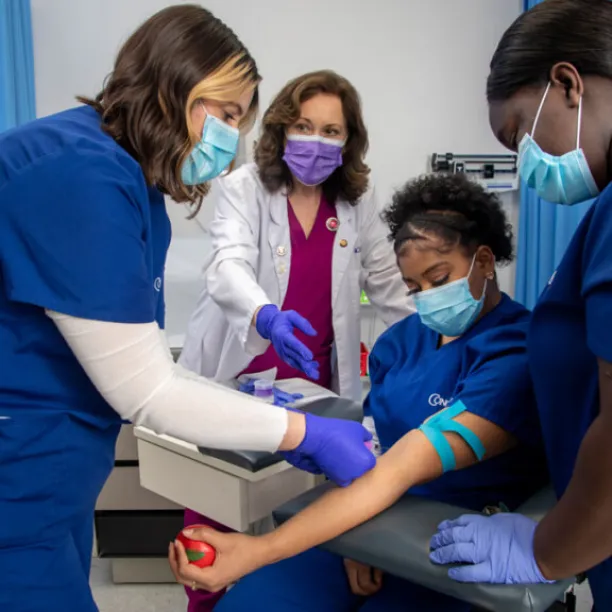 Medical assistant students practicing phlebotomy skills during hands-on training in a clinical education lab setting.