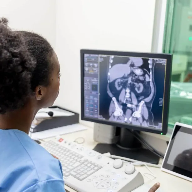Radiologic technologist analyzing abdominal CT scan on monitor in a medical imaging control room.