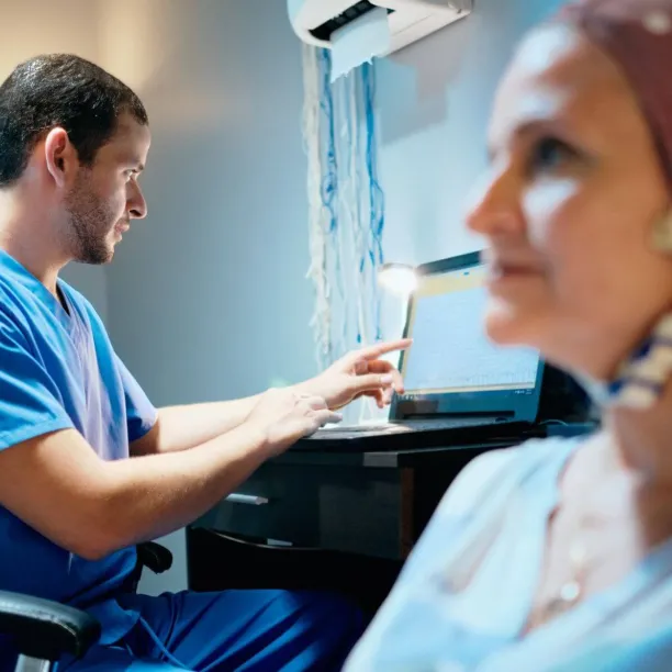 EEG technician monitoring brain wave activity on screen while patient undergoes neurological testing in clinical setting