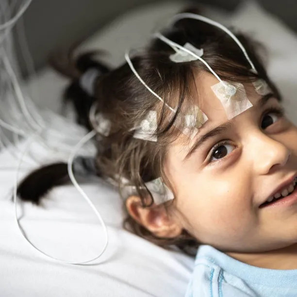 Smiling child with electrodes attached during a sleep study, representing the role of a polysomnographer in monitoring pediatric sleep patterns