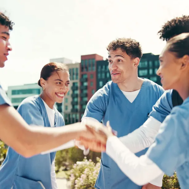 A group of nursing students in scrubs standing together and offering each other encouragement and peer support.