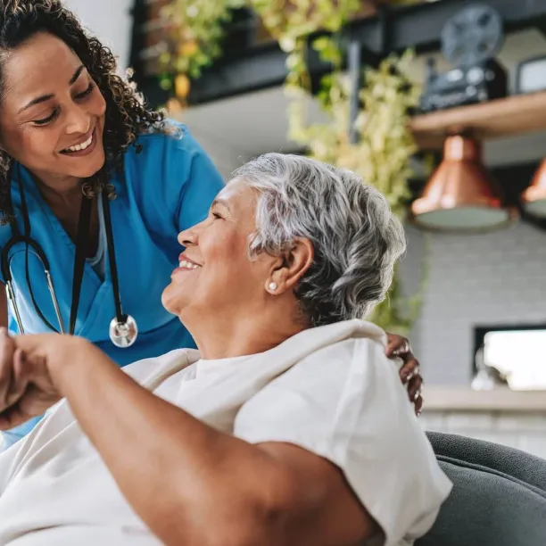 A smiling nurse holds the hand of an elderly patient in a warm, bright room, illustrating the rewarding patient-care aspect of changing your career to nursing.