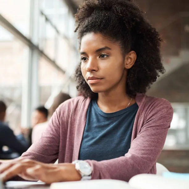 A focused young woman using a laptop in a bright study area to research FAFSA deadlines and submit her financial aid application online.