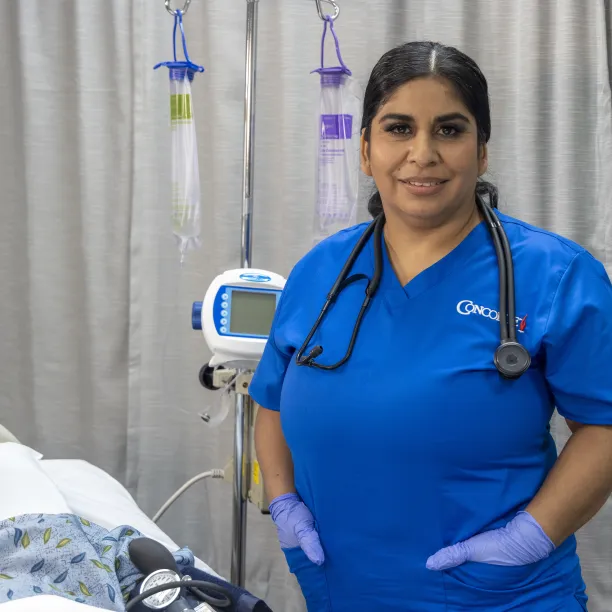 A female nurse with dark hair and blue scrubs poses for camera in lab setting