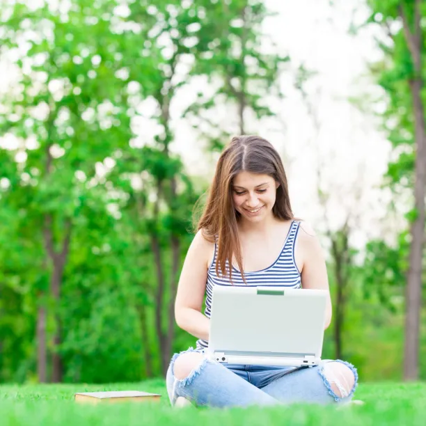 female teenager high school graduate researching on laptop outside during summer