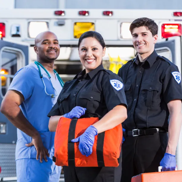First responders, two paramedics and a healthcare worker, pose in front of and ambulance