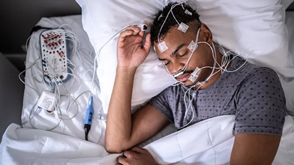 A sleep study patient sleeps in a bed while connected to electroencephalography equipment that detects brain activity during a sleep study.