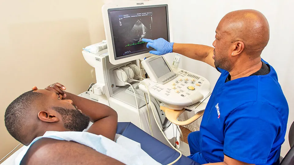 Cardiac sonographer with patient points to image on screen. Cardiac sonographer with patient points to image on screen.