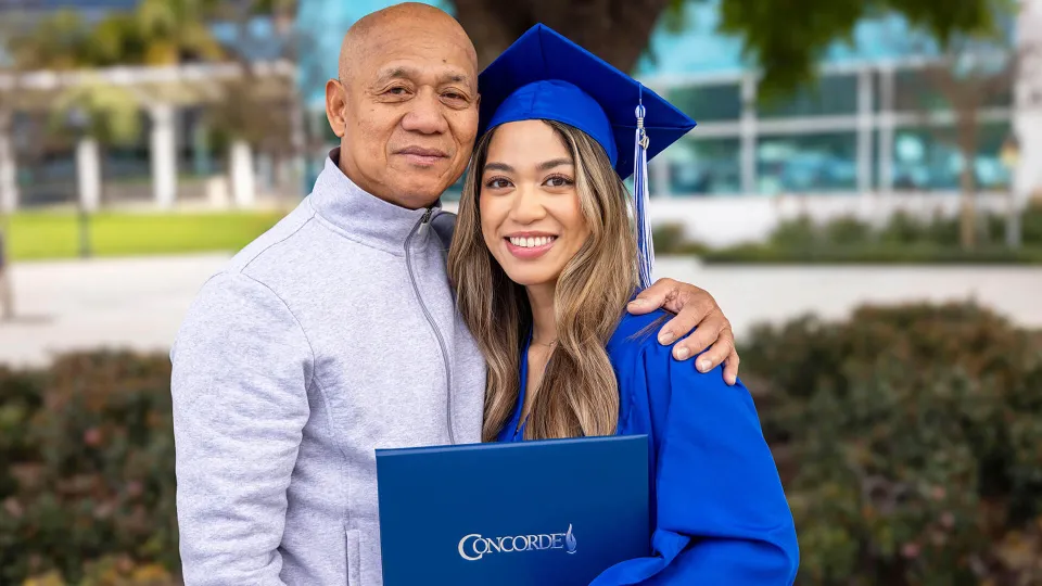 Concorde graduate wearing cap and gown holds degree and poses with proud family member.
